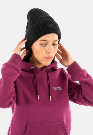 Sort strikket hue med ribbet tekstur, der har en rund top og tætsiddende pasform, båret af en person iført en bordeaux hættetrøje.