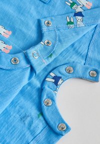 Gros plan sur une grenouillère bleue pour bébé avec des boutons-pression en métal et un motif lapin de dessin animé sur un tissu doux.