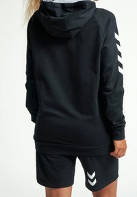 Svart huppartröja med grått innerfoder, med vita chevronränder på ärmarna. Matchas med svarta shorts i samma stil.