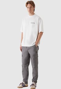White short-sleeve t-shirt with "PROHIBITED" text on chest, paired with gray cargo pants featuring multiple pockets and a streamlined fit.