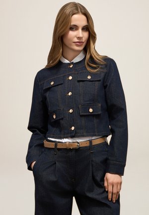 Chaqueta de mezclilla en azul oscuro con un diseño corto, que cuenta con dos bolsillos en el pecho, botones dorados y un cuello liso sobre una camisa blanca.