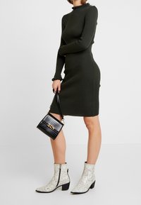 Grön randig klänning med hög hals och volangärmar, tillsammans med vita ankelboots i ormskinnsmönster och en liten svart handväska med textur.