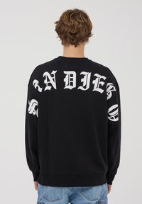 Felpa nera con grande scritta bianca "INDIES" sul retro e scritte stilizzate sulle maniche. Materiale in cotone, vestibilità rilassata e polsini a costine.
