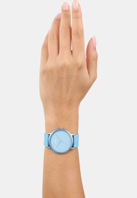 Lichtblauw horloge met een gladde siliconen band en een ronde metalen kast. De wijzerplaat heeft minimale markeringen en zilveren wijzers.