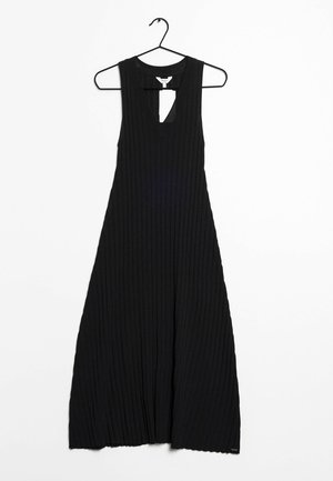 Zwarte geribde maxi-jurk met een mouwloos ontwerp en een kleine uitsparing bij de hals. Hangt aan een zwarte haak op een witte achtergrond.