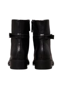 Paire de bottines en cuir noir montrées de dos avec des fermetures éclair et des sangles décoratives autour des chevilles.