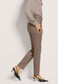 Braune karierte Hosen mit maßgeschneidertem Schnitt, die eine glatte Textur und seitliche Taschen aufweisen, kombiniert mit schwarzen Slingback-Absätzen mit spitzem Zehen.