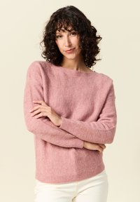 Rosa fiskbenstickad tröja med boxig form, bred halsringning och ribbade manschetter, parat med ljusa byxor. Mjuk textur.