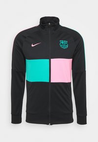 Chaqueta negra con cremallera, con paneles horizontales en tonos verde azulado y rosa. Presenta el logo de Nike y el emblema de Barcelona. Fabricada con material suave y transpirable.