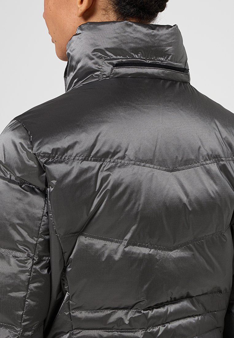 Persona vestida con una chaqueta de plumas brillante de color gris oscuro, con un alto cuello y un bolsillo con cremallera horizontal en la parte trasera del cuello.