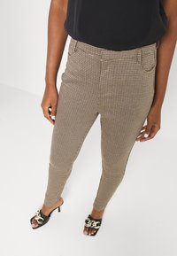 Bruine houndstooth-gepatroniseerde skinny broeken met voorzakken en een hoge taille, gecombineerd met zwarte hoge hakken sandalen met een kettingaccent.