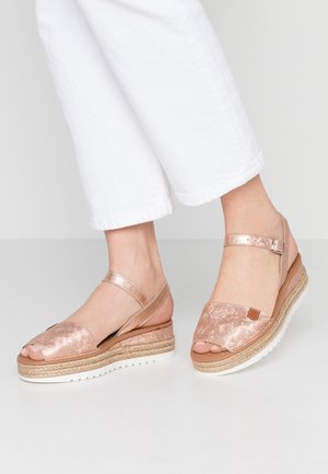 Różowo-złote sandały na koturnie z teksturowaną cholewką, otwartym toe i regulowanym paskiem wokół kostki. Podeszwa z juty i gumy dla lepszej przyczepności i komfortu.