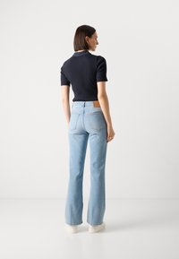Jeans acampanados azules de mezclilla, con una cintura alta y un parche de cuero marrón en la parte posterior. Combinados con una blusa ajustada de canalé azul marino.