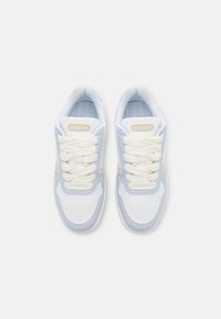 White and light blue sneakers with a textured leather upper, cream laces, and a simple design. Lacoste logo on the tongue.