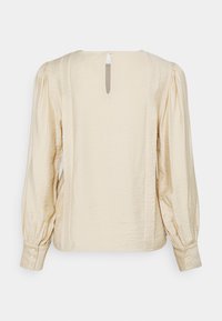 Blusa di seta crema con maniche lunghe a bolla, polsini bottonati e apertura a occhiello sul retro. Texture liscia con un leggero lucido.