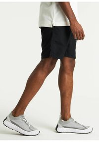 Pantaloni corti neri con cuciture laterali; abbinati a scarpe sportive grigie con tomaia testurizzata e suola bianca. Vestibilità comoda, design casual.
