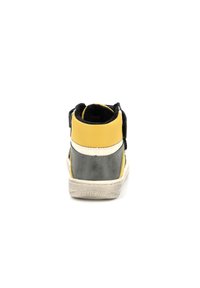 Zapatilla de caña alta con parte superior en amarillo y negro, talón gris, franjas blancas de acento y superficie texturizada. Cierre de velcro en la parte superior.