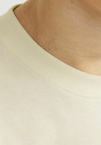 T-shirt in cotone di colore beige chiaro, con collo rotondo e texture morbida, dettagli sul colletto a coste.