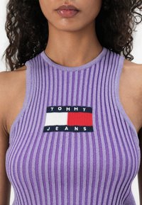 Lilla ribbet tanktop med et sentralt brodert Tommy Jeans-logo med blå, hvite og røde detaljer. Figurformet design med høy hals.