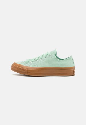 Lavtop sneaker i lysegrønt ruskind med brun gummisål og matchende brun tåhætte, set fra siden på hvid baggrund.