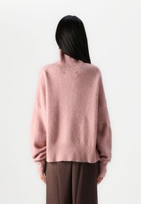 Rosa, übergroßer, gestrickter Pullover mit hohem Kragen und geripptem Saum. Weiche Textur mit leichtem Flaum. Lange, überschnittene Ärmel.