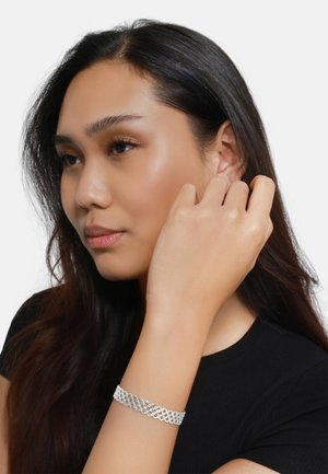 Zilveren mesh armband met een ingewikkeld lattice-ontwerp, gedragen om een pols, tegen een neutrale achtergrond. Glad, reflecterend oppervlak.