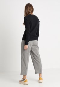 Svart ribbad långärmad topp kombinerad med rutiga vida byxor och flerfärgade sneakers, som visar en avslappnad outfit bakifrån.