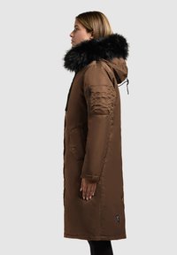 Brun parka med en faux fur hætte, lynlåse og trykknap lommer, lige snit og tekstureret stof, præsenteret fra siden.