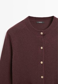 Cardigan a maglia color borgogna con scollatura rotonda, cinque bottoni in tonalità oro e finitura textured. Il tessuto appare morbido e caldo.