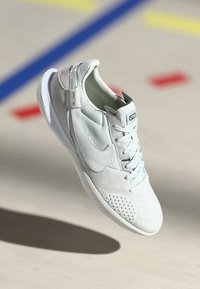 Világosszürke sportcipő textúrált felsőrésszel, perforált részletekkel, sima talppal és kiemelkedő logóval az oldalon.