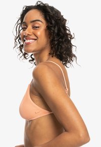 Lys ferskenfarget ribbet bikini topp med smale justerbare stropper og et merke-logo. Har trekantet snitt og teksturert materiale.