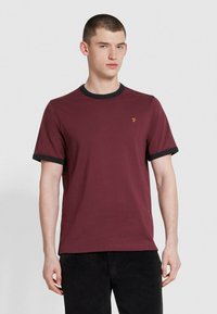 T-shirt in cotone borgogna con colletto e polsini delle maniche a coste neri. Presenta un piccolo logo giallo sul petto. Maniche corte, forma rotonda.