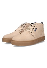 Beige suede ankle boots with rounded toes, lace-up design, and a textured rubber sole. Features a navy accent tag and striped rear pull tab.