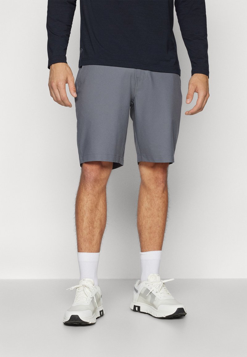 Menns grå sporty shorts med en glatt tekstur, over knelengde, kombinert med hvite sneakers og ankelsokker.