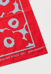 Rode katoenen sjaal met grote blauwe bloemenpatronen en witte accenten, met een gedrukt logo en tekst die het merk en de productiedatum aangeven.