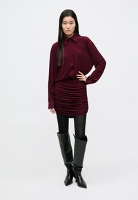 Bordo spalvos palaidinė su smailiu apykakliu, derinama su raukšlėtu sijonu. Juodi odiniai aulinukai iki kelių, laisvo silueto, su smailiomis noselėmis. Juodos pėdkelnės.