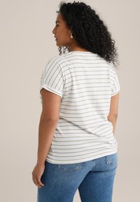 T-shirt a righe a maniche corte bianco con strisce color sabbia, con maniche arrotolate e vestibilità rilassata, abbinato a jeans blu.