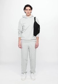 Hanorac gri și pantaloni de trening cu o potrivire lejeră, asortați cu o geantă neagră tip crossbody și adidași albi. Textură netedă și design minimalist.