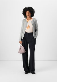 Light gray cardigan over a cream blouse with orange floral print, paired with dark navy trousers and a small light purple bag.