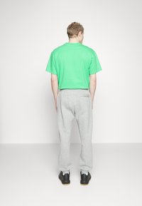 Grön bomullströja med avslappnad passform, tillsammans med grå joggingbyxor, elastiska ärmslut och svarta skor. Utsikt från baksidan med en enkel bakgrund.