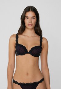 Schwarzer Spitzen-BH mit gepunktetem Netz, unterstützt durch Unterbrustbügel, mit gewellten Kanten und verstellbaren Trägern. Passender Spitzen-Slip mit ähnlichen Details.