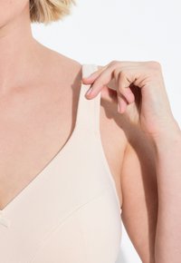 Beige soft-cup beha met verstelbare bandjes. Kenmerkt zich door een zachte stof, subtiele stiksels en een klein strikdetail aan de voorkant.