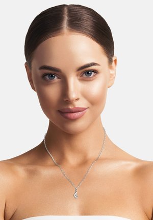 Collana in argento con pendente a forma di nota musicale. Il design è elegante con una finitura lucida, esibita su un collo nudo.