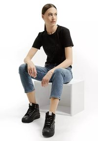 Czarna bawełniana koszulka z minimalistycznym wzorem, niebieskie dżinsy oraz czarne trampki za kostkę z teksturowanymi akcentami i białą naszywką z logo.