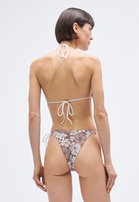 Hnedé kvetinové bikini s bielymi šnúrkami na krku a chrbte. Textúra je hladká a vzor obsahuje biele kvety.