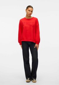 Rotes Sweatshirt mit dem Text "LOS ANGELES", lässiger Schnitt, runder Ausschnitt und langen Ärmeln, kombiniert mit dunkelblauen Jeans und Turnschuhen.