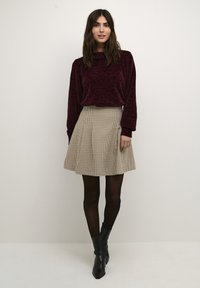 Pull en maille texturée bordeaux avec un col cheminé, associé à une jupe évasée à carreaux beige et noir et des bottines noires.