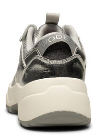 Grå sneaker med en blank metallisk ovandel, texturerad detaljering och en vit mellansula. Har en hälflik och varumärket "WODEN" på remmen.