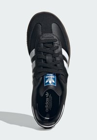 Čierne tenisky so zvrškom z semišu a kože, s tromi bielymi pruhmi, čiernymi šnúrkami a modrým logom Adidas na jazyku. Hnedá gumová podrážka.
