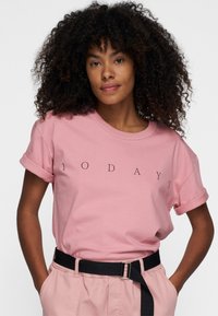 T-shirt in cotone rosa con maniche corte arricciate, caratterizzata da testo stampato in nero "10 DAYS" in un font moderno. Texture liscia, vestibilità rilassata.